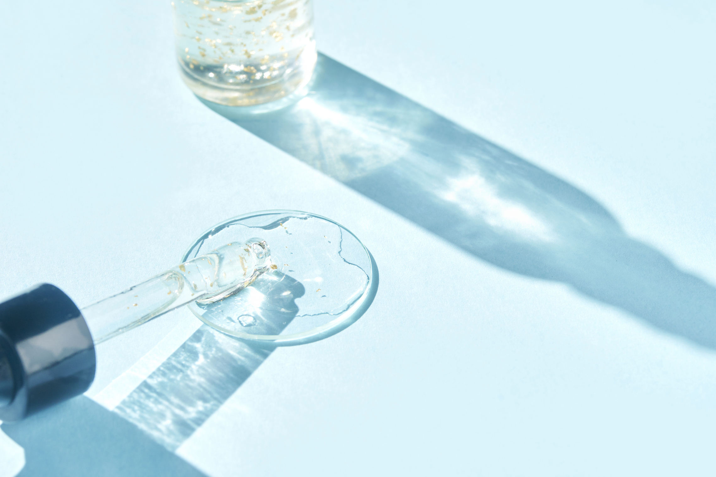 Serum gel texture swatch. Transparent drop with golden sparkles. Blue background